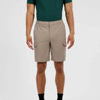 A man wearing beige cargo shorts with side flap pockets, paired with a dark green polo shirt and black socks, shown from the chest down against a light gray studio background.