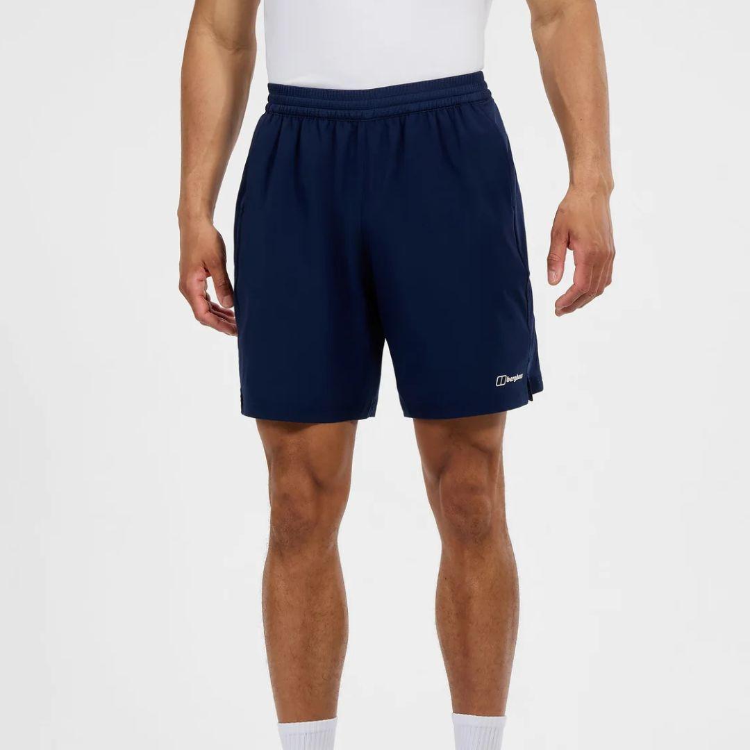 A person wearing navy athletic shorts with a white Berghaus logo on the lower left hem, paired with a white top and white socks, shown against a light gray studio background.