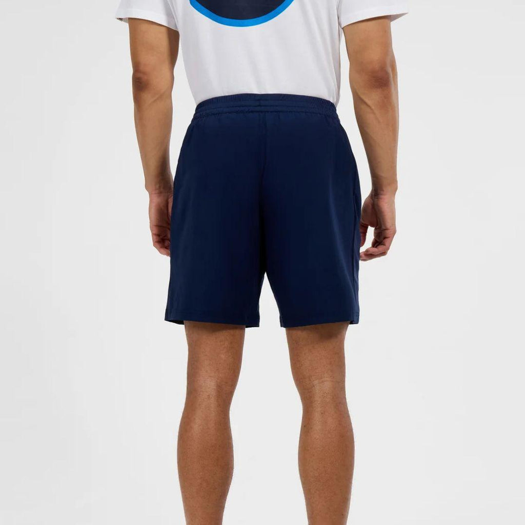 A man viewed from the back wearing navy blue athletic shorts and a white t-shirt with a blue graphic, against a plain light gray background.