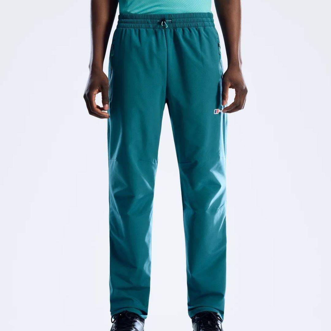 A person wearing teal Berghaus pants with an elastic drawstring waist and a small white logo on the left thigh, shown against a light gray studio background.