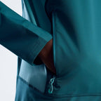 Close-up of a teal athletic jacket with a side zipper and pocket, showing a hand reaching into the compartment against a light gray background.