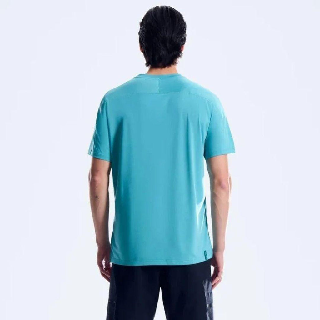 A man viewed from behind wearing a short-sleeve athletic t-shirt in a vibrant turquoise blue color, paired with black pants, against a clean white studio background.