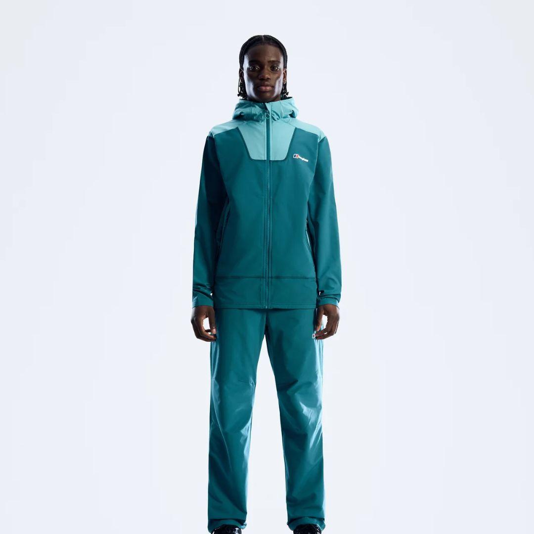 A model wearing a matching Berghaus teal and light blue outdoor tracksuit with a hooded jacket and pants, standing against a plain white studio background.