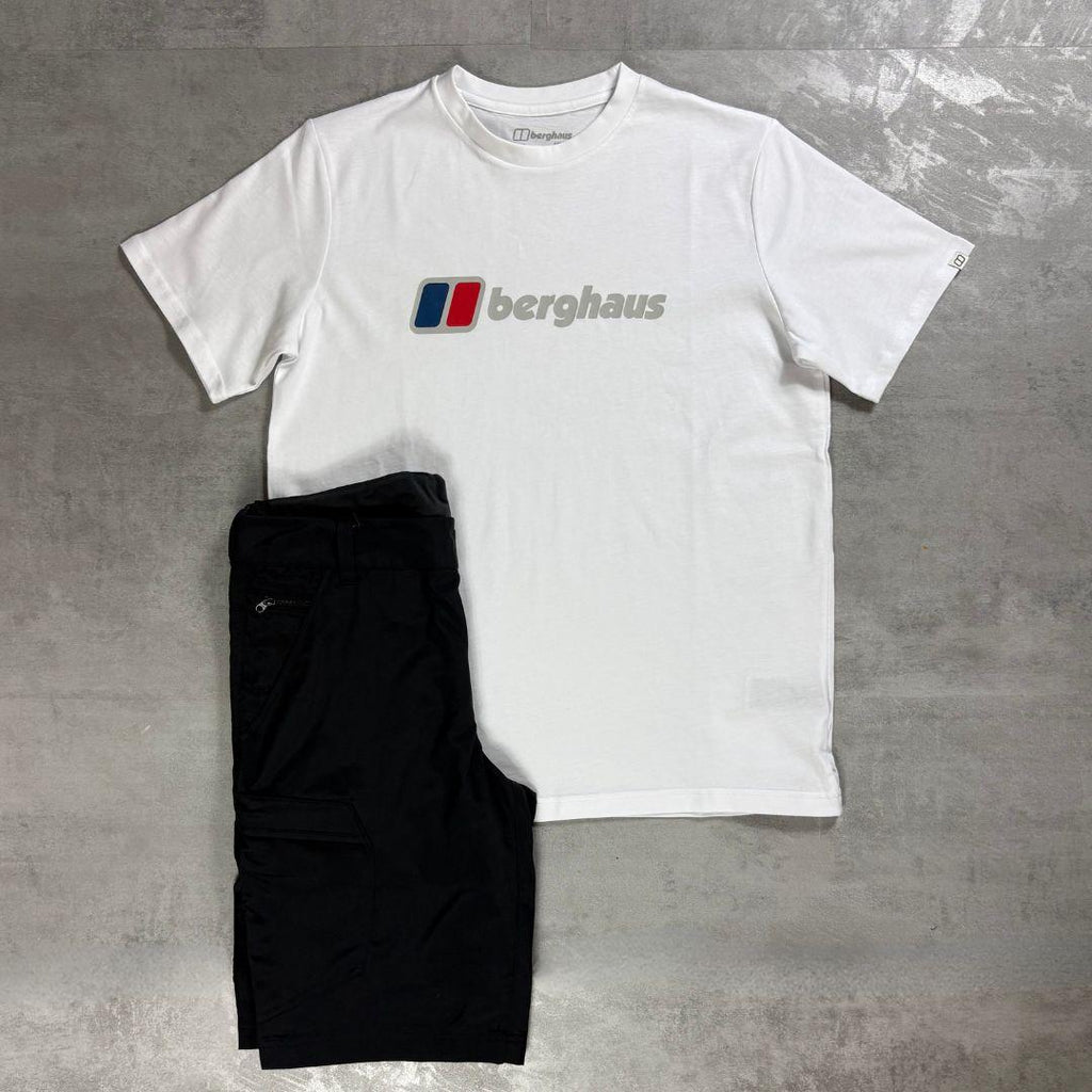 A white Berghaus short-sleeve t-shirt with the brand's logo printed on the chest, laid flat on a gray concrete surface next to a pair of black cargo pants.