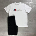 A white Berghaus short-sleeve t-shirt with the brand's logo printed on the chest, laid flat on a gray concrete surface next to a pair of black cargo pants.