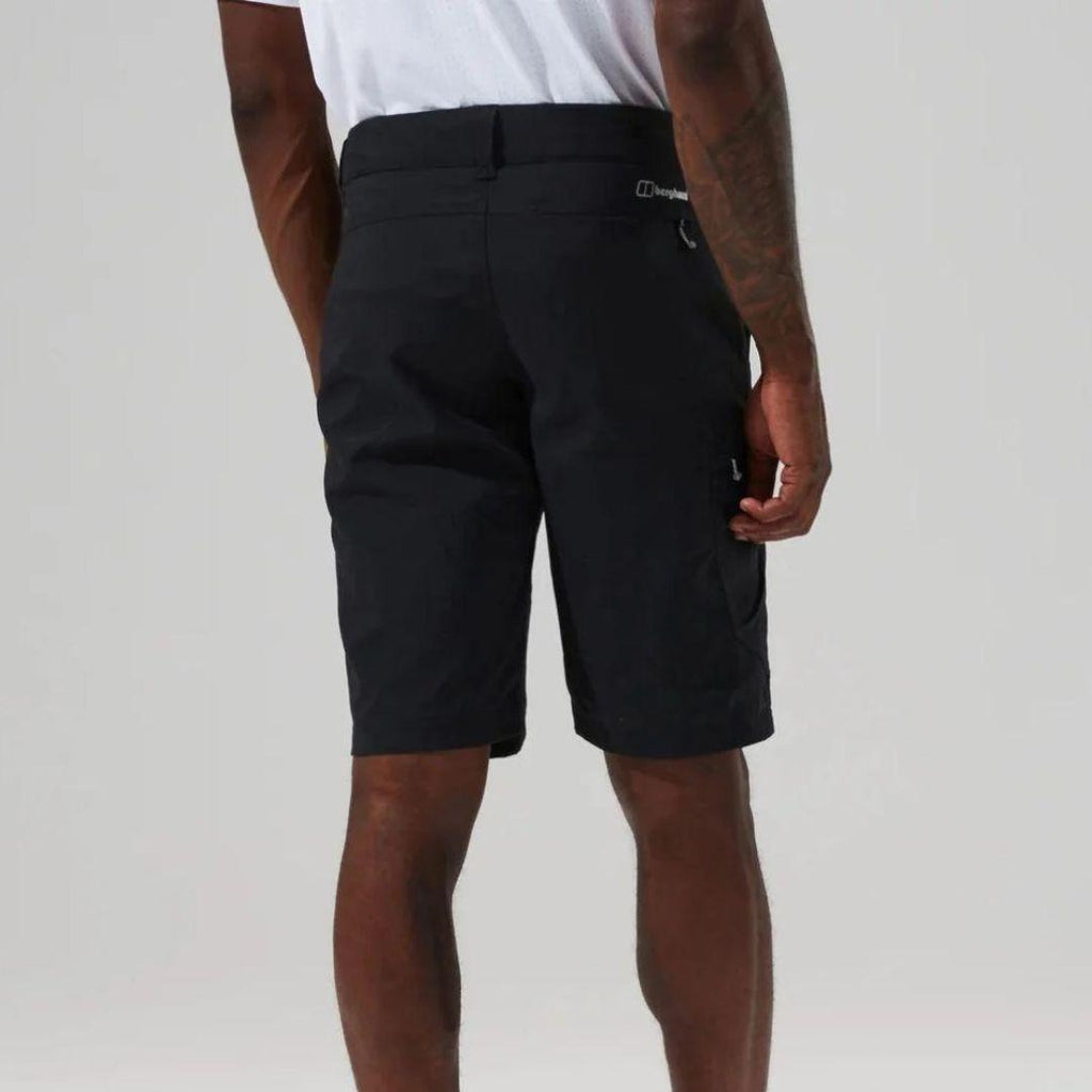 A man wearing black cargo shorts and a white t-shirt, shown from the back against a light gray studio background. The brand name 'Berghaus' is visible on a small white tag on the back pocket.