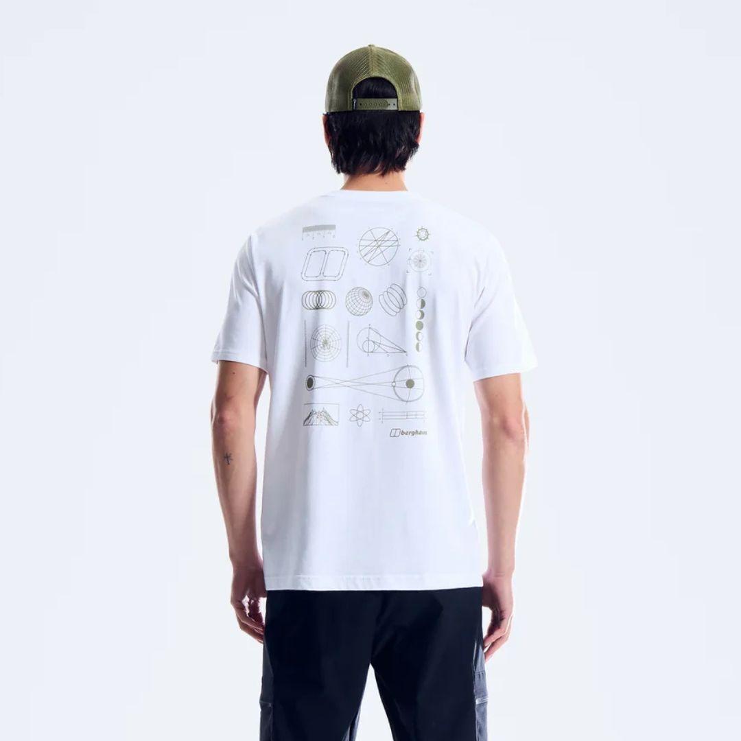 A man viewed from behind wearing a white t-shirt with a geometric line-art graphic print on the back, paired with black pants and an olive green baseball cap against a light gray studio background.