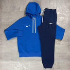 Nike Blue Club Fleece Hoodie and Joggers Tracksuit for men, flat lay of royal blue cotton fleece pullover hoodie with white drawcords and kangaroo pocket and matching navy cuffed joggers with white Nike swoosh