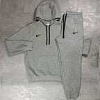 Nike Grey Club Fleece Hoodie and Joggers Tracksuit for men, flat lay of marl grey cotton fleece pullover hoodie with drawcord hood and kangaroo pocket and matching cuffed joggers with black Nike swoosh