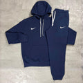 Nike Navy Club Fleece Hoodie and Joggers Tracksuit for men, flat lay of navy cotton fleece pullover hoodie with white drawcords and kangaroo pocket and matching cuffed joggers with white Nike swoosh