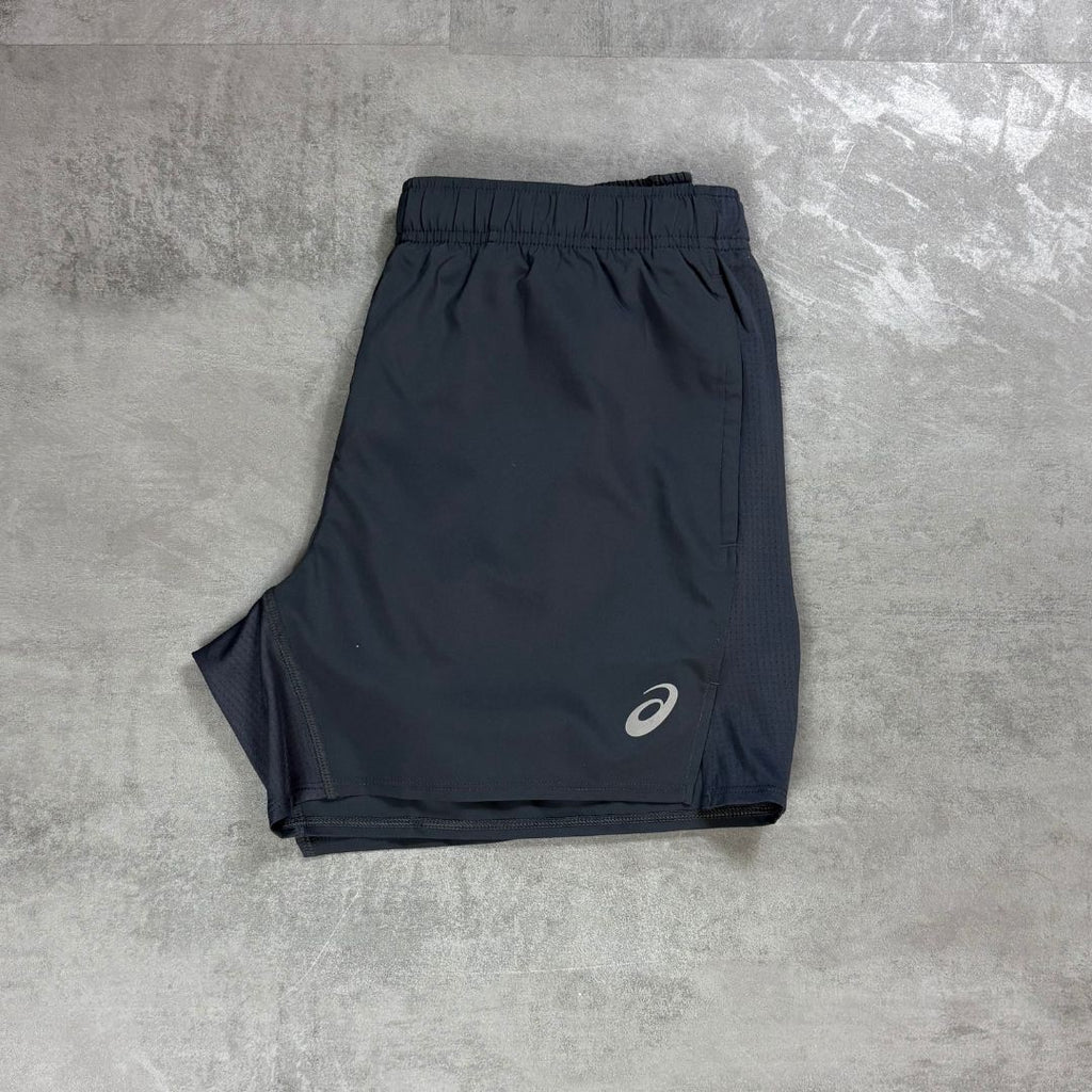 Grey athletic shorts with an elastic waistband and a small white Asics logo on the lower left leg, laid flat on a gray textured surface.