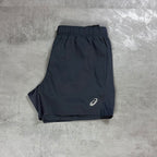 Grey athletic shorts with an elastic waistband and a small white Asics logo on the lower left leg, laid flat on a gray textured surface.