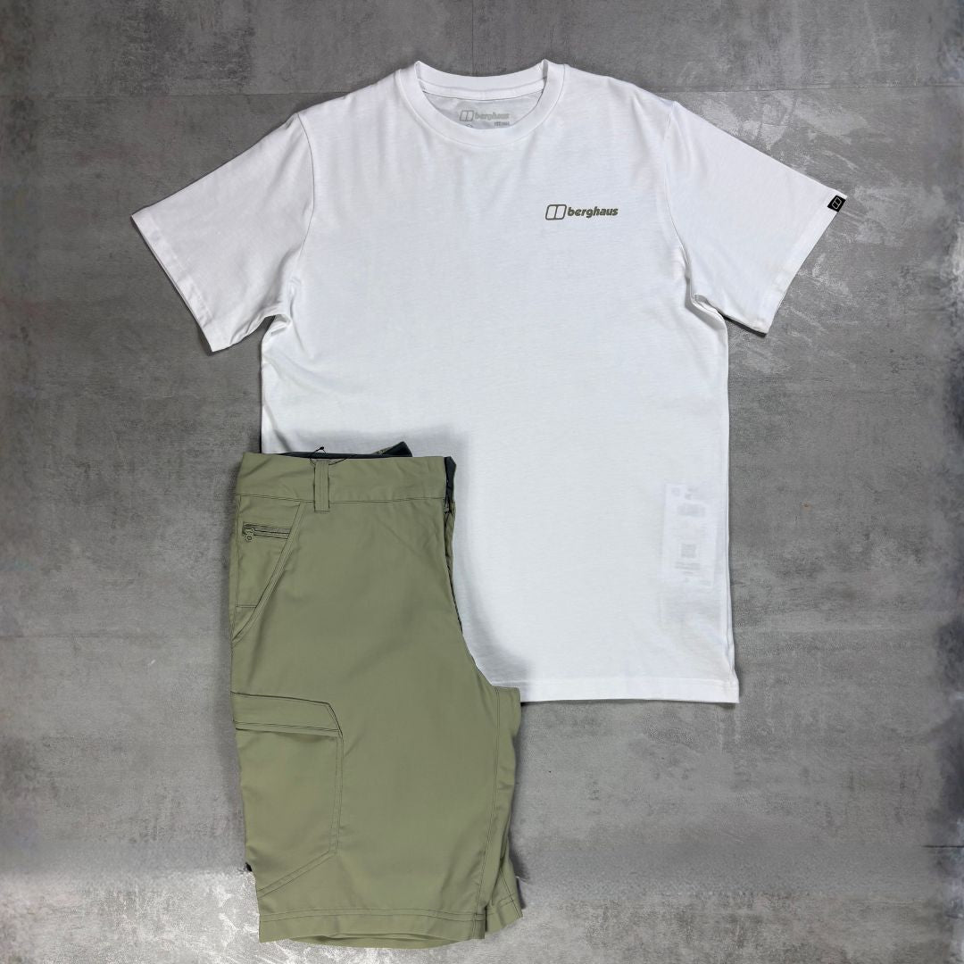 A white short-sleeve crewneck t-shirt with a small black Berghaus logo on the left chest, laid flat next to a pair of olive green cargo shorts on a textured gray concrete background.